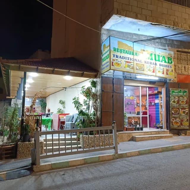 Night exterior of Restaurant Muab in Karak, Jordan, displaying a sign for traditional Kerak dishes, with an open patio and street view.