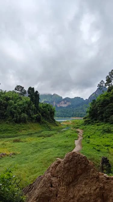 A dirt path winds through a lush green valley toward distant mountains and a lake under a cloudy sky in the Namosi highlands.