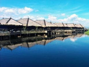 Wooden stilt houses of a luxury resort overlooking Inle Lake, with boats moored nearby