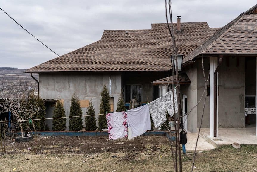 Rural house exterior with laundry hanging on a line, bare trees, and overcast sky in Moldova