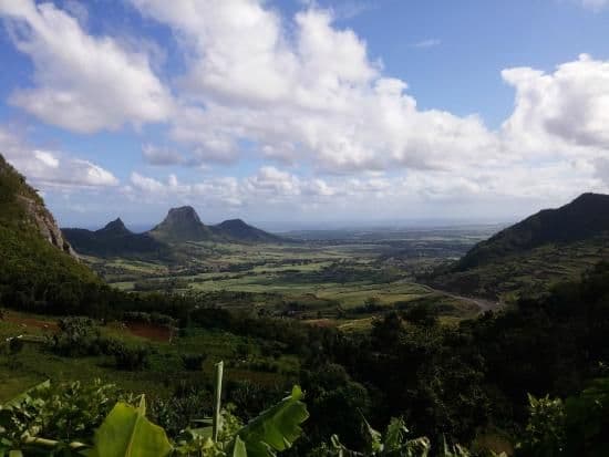 Aerial landscape view of lush green mountains and coastal plains under a blue sky with scattered clouds.