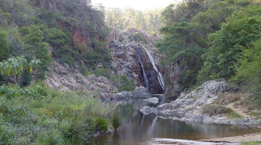 A small waterfall cascading over rocky cliffs into a calm pool in the Nsoko area of Eswatini, surrounded by dense green forest and vegetation.