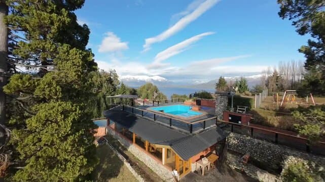Aerial view of a lakeside property with a rooftop pool, overlooking a large lake and snow-capped mountains under a blue sky.