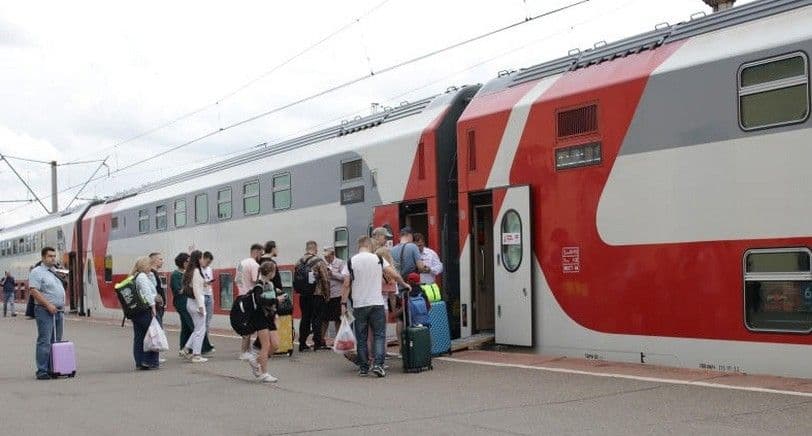 Passengers with luggage board a red and white regional train at a station platform on the North Caucasus Railway serving Krasnodar Krai.