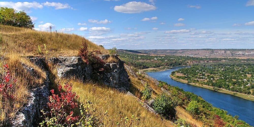 Wide landscape photograph of a rocky hillside with autumn grasses and red foliage overlooking a winding river near Ocnița