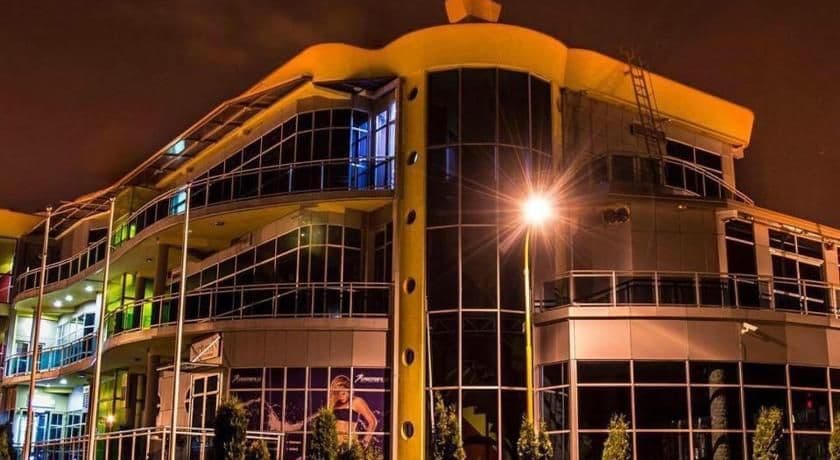 Nighttime exterior of a modern multi-story building with illuminated windows, balconies, and a bright street lamp in Derventa.