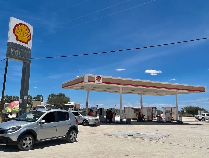 Shell fuel station exterior in Okahao, Ongandjera, with pumps, canopy, and parked cars under a clear blue sky in a remote setting.