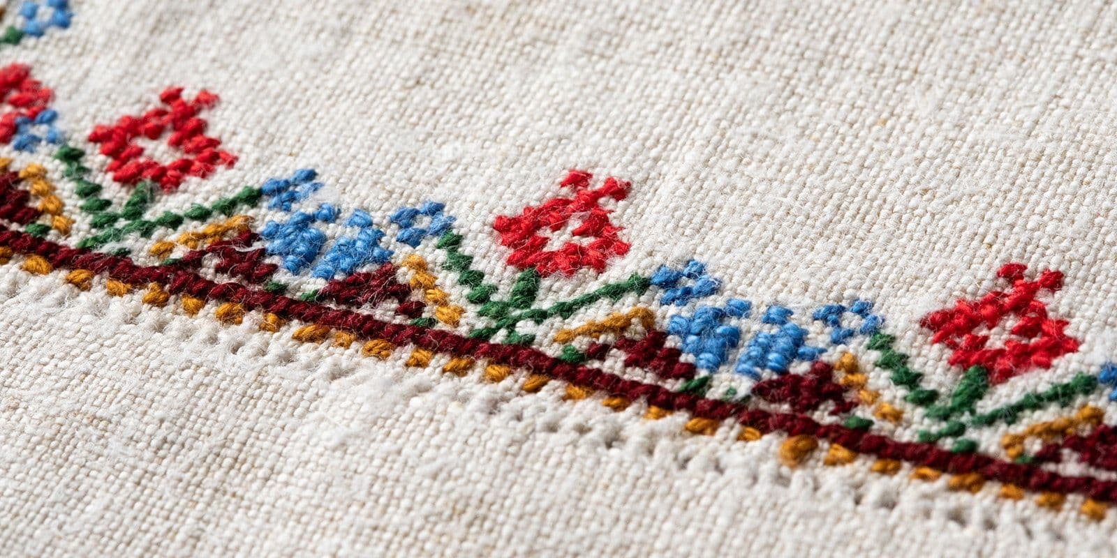 Close-up macro shot of traditional Hungarian folk embroidery featuring red and blue floral motifs on white linen fabric.