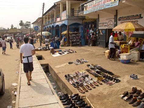 Busy street market scene in Bo, Sierra Leone, with vendor stalls, pedestrians, and storefronts along the road.