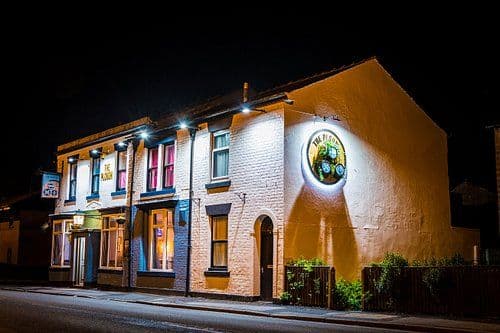 Night exterior of The Plough pub in Euxton, a brick building with illuminated signage and windows on a quiet street.