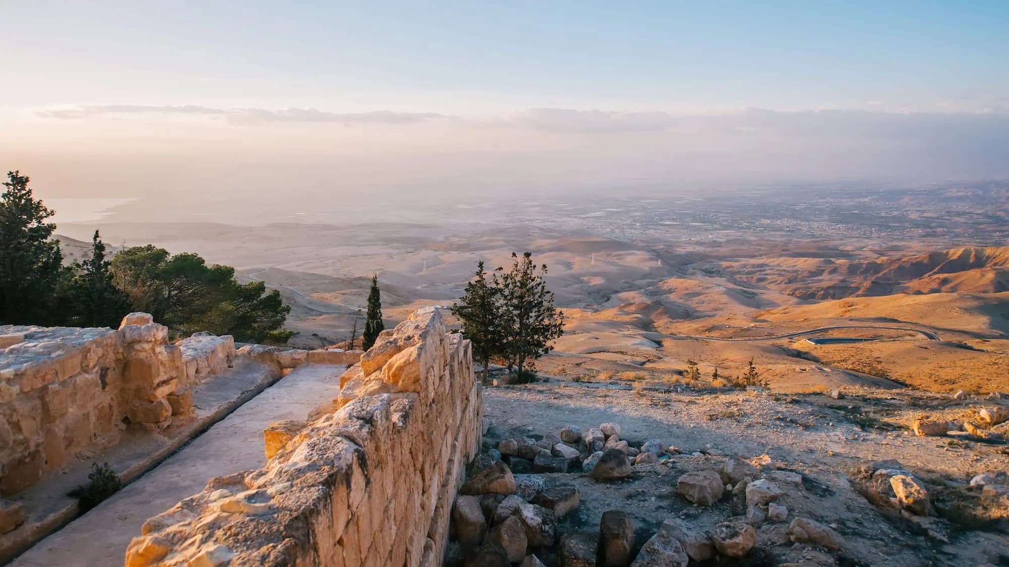 Elevated view over open Karak terrain in Jordan with stone ruins, scattered trees, and soft golden light.