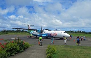 Small propeller plane parked on a tarmac at Tanna Island airstrip, Isangel, Vanuatu, with greenery and a partly cloudy sky