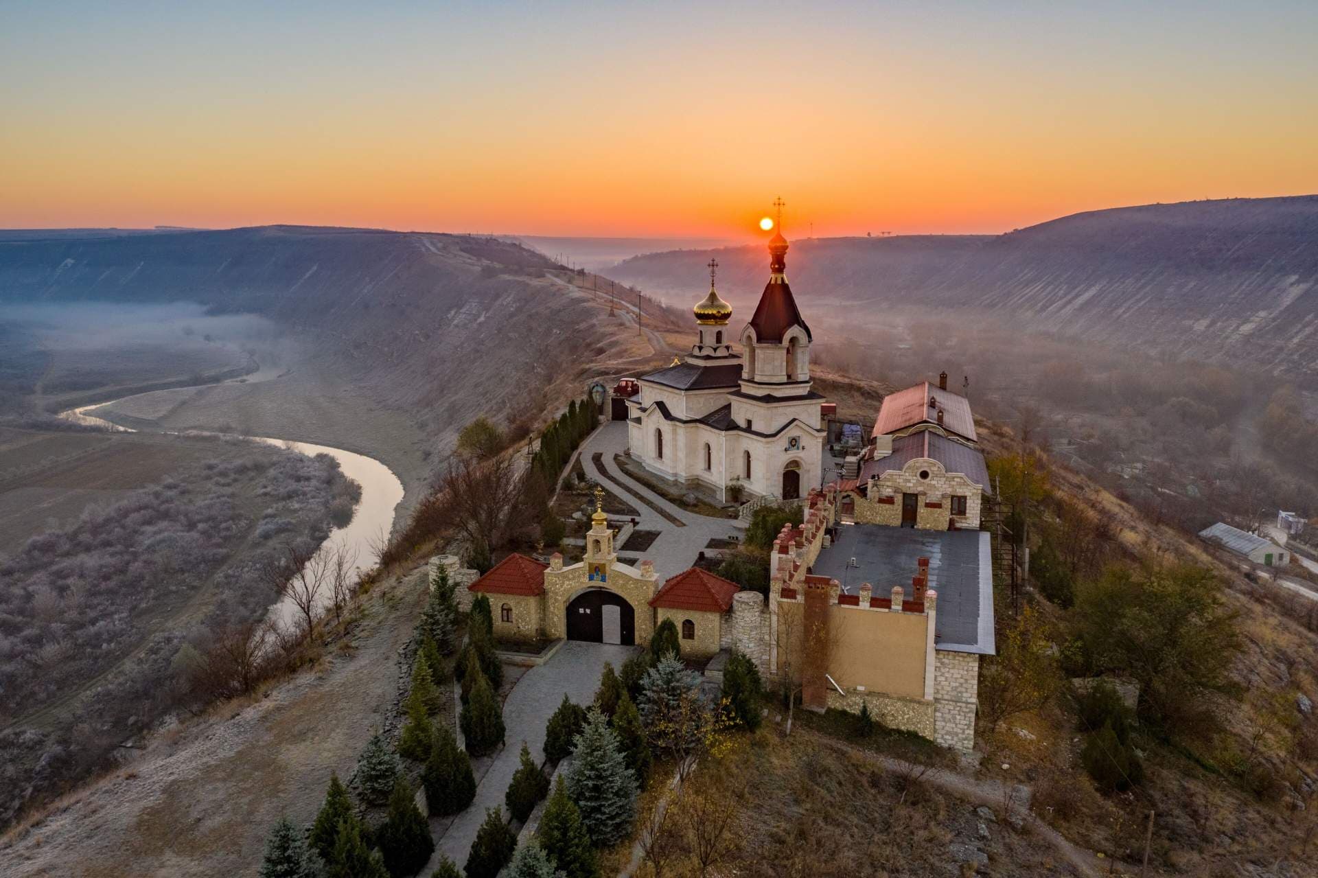 Aerial view of a hilltop Orthodox church complex overlooking a misty river valley at sunset in Moldova