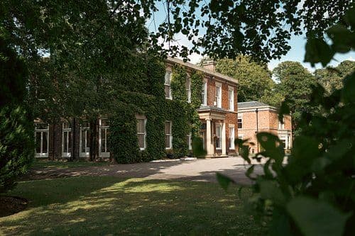 Exterior of a Georgian-style country house with ivy-covered brick facade, set in a landscaped garden with mature trees near Euxton.