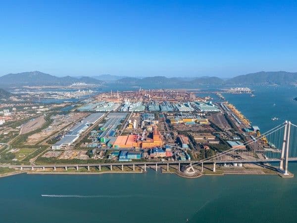 Aerial view of a large industrial port complex and suspension bridge in Gwangyang-si, with mountains and water in the background