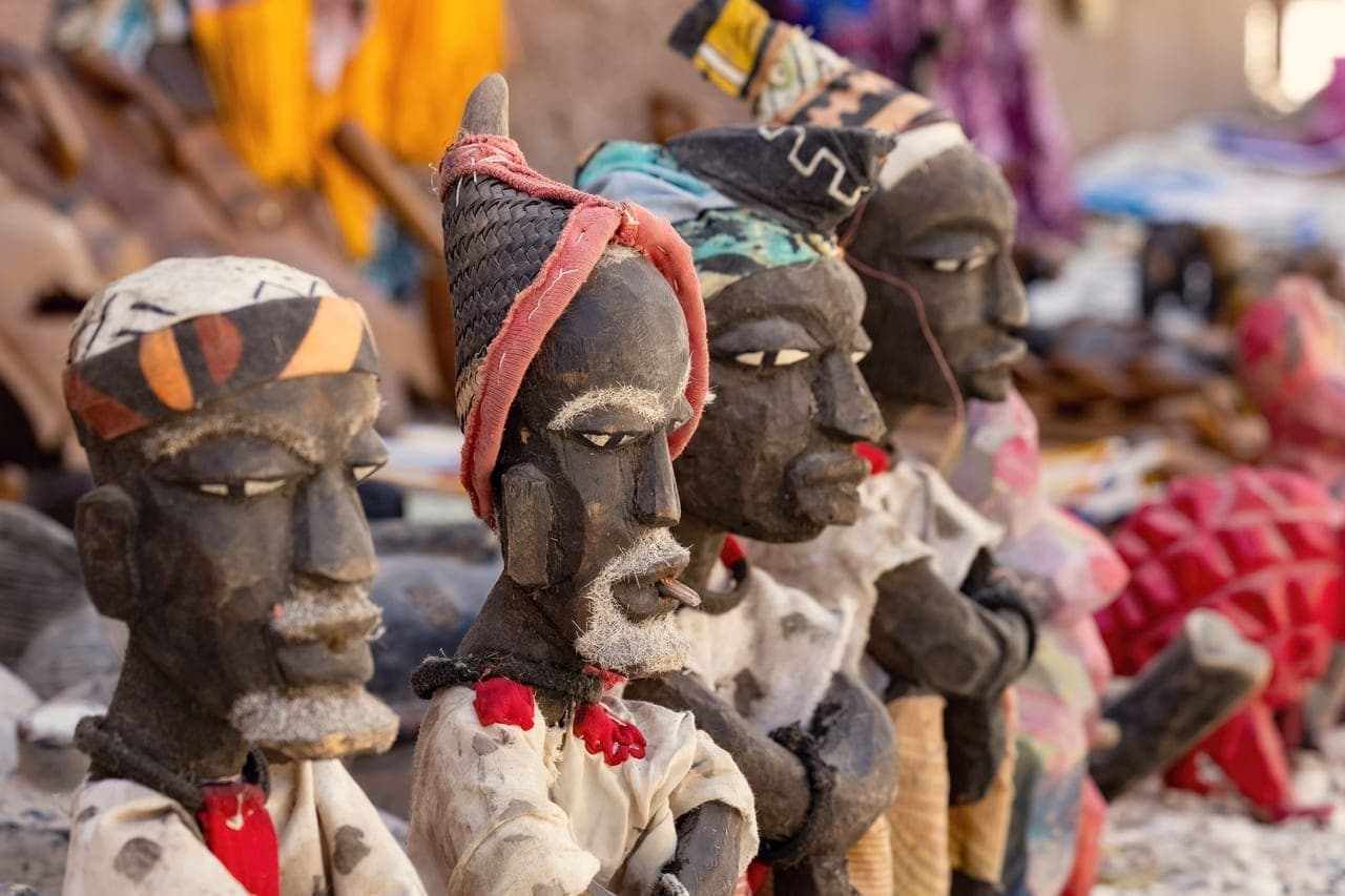 Oussouye street market with traditional wooden statues and colorful vendor stalls along a paved road