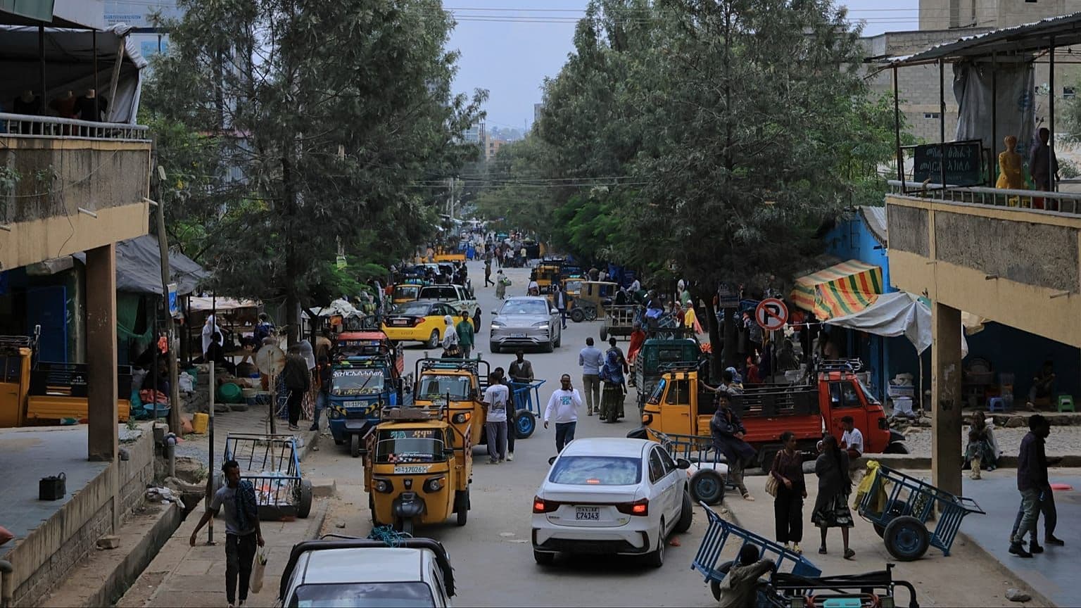 Busy street scene in the Afar Region with auto-rickshaws, cars, pedestrians, and roadside market stalls.